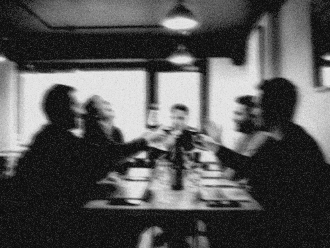 Blurred black-and-white photo: a group toasting in a wine bar, laptops on the table