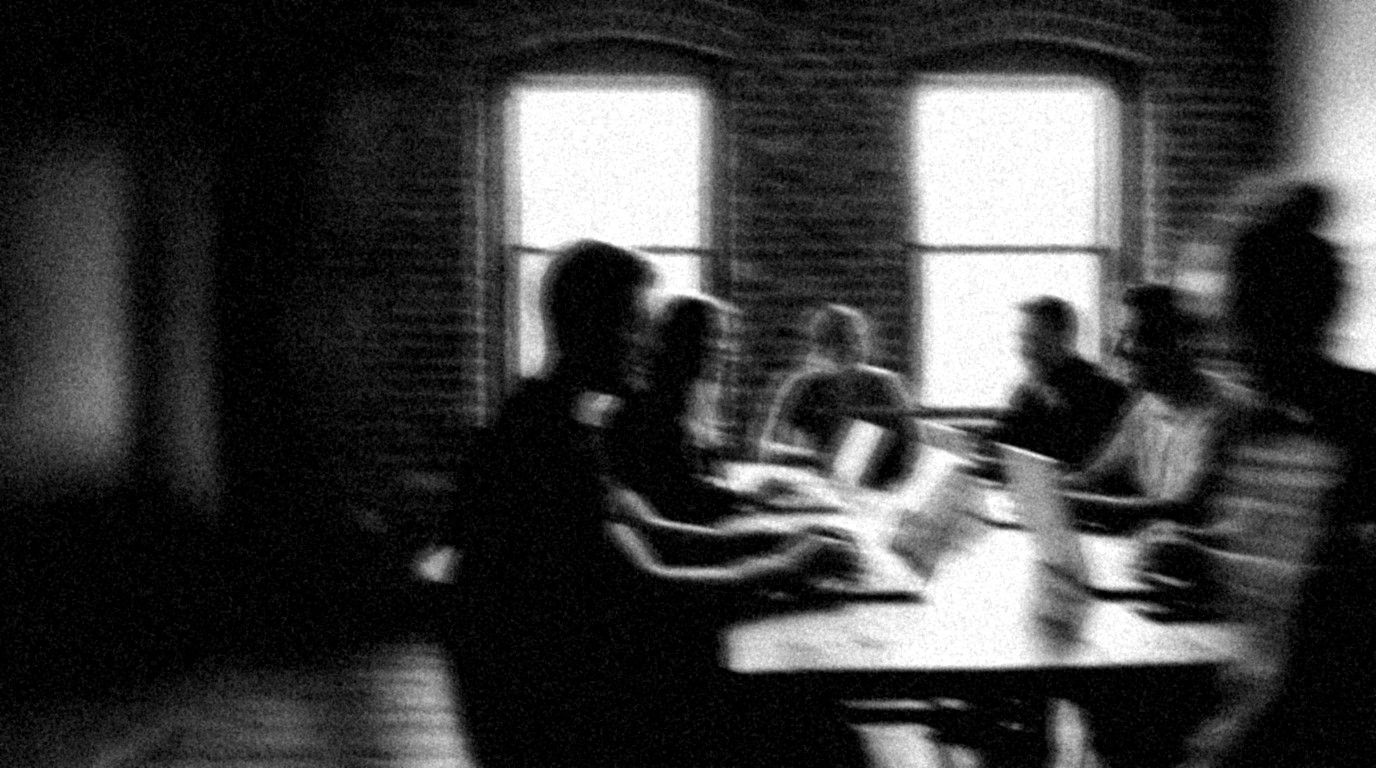 Blurred black-and-white photo: a group at laptops in a bright loft, two people leaning toward each other